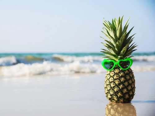 Ananas med solbriller i vandkanten på en strand